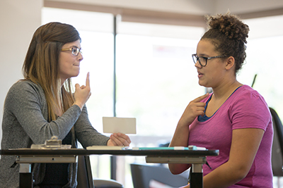 Female speech therapist pointing to mouth and female patient attempting to mimic