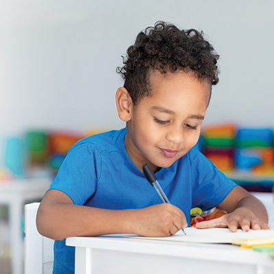 A young boy happily writing at his desk