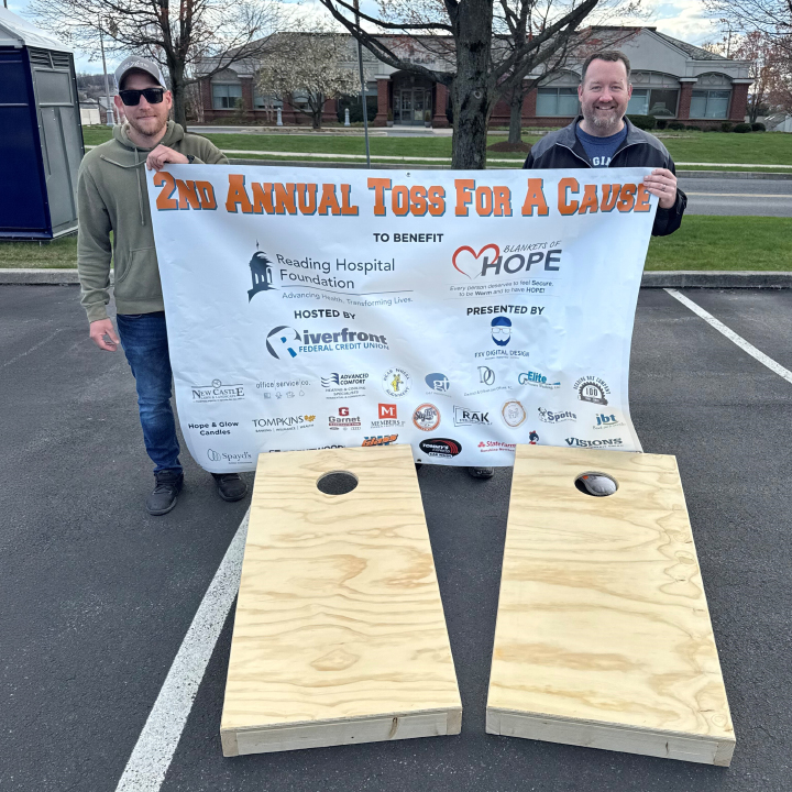 Two individuals hold up a sign for the Toss for a Cause fundraising event.
