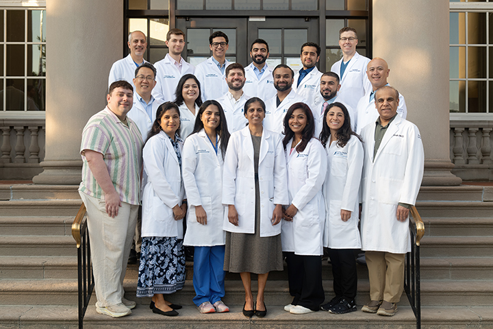 Pulmonary Disease and Critical Care Medicine Fellowship faculty and fellows dressed in white coats posing on steps in front of hospital entrance