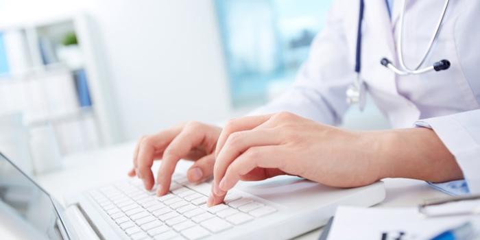 person wearing white lab coat with hands typing 