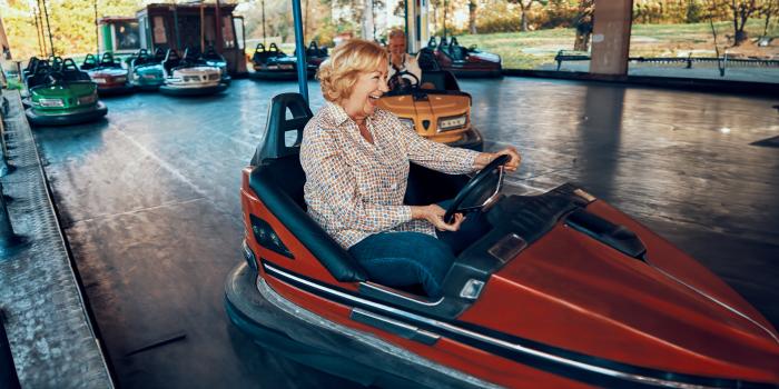 An older woman joyfully able to ride bumper cars at the park after her hip replacement.