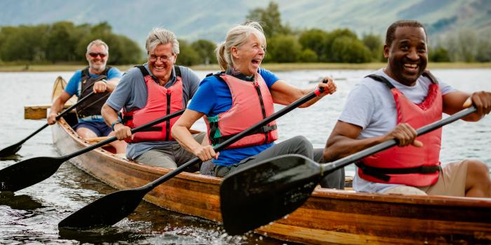 A group of 4 older adults laughing while rowing a canoe together, happy to regain mobility after shoulder replecment.