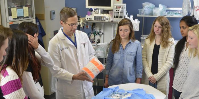 Doctor in lab coat next to hospital bed showing medical equipment to students