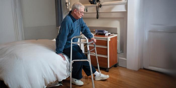 A person stands a edge of sitting location, and reaches one hand back to grip arm of chair or bed. Next other hand reaches back to begin sitting.